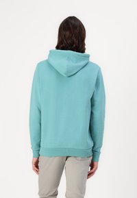 Jasnoniebieska bawełniana bluza z kapturem, z kieszenią kangurką, ściągaczami na mankietach i u dołu oraz regulowanym kapturem. Prosty design, bez widocznych logotypów ani wzorów.