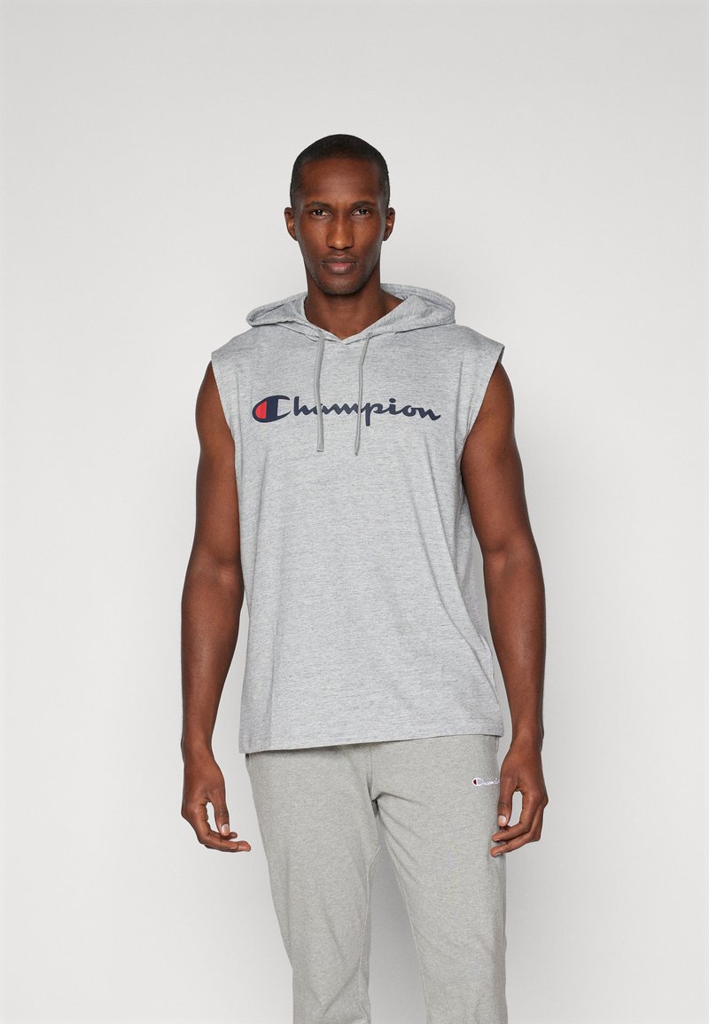 Grijze mouwloze hoodie met een voorktas, voorzien van het 'Champion' logo in marineblauw en rood. Zachte textuur, casual pasvorm, gecombineerd met lichtgrijze broek.