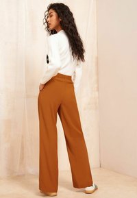 Brede, hoge taillebroek in een warme oranje kleur, gemaakt van een zachte stof; voorzien van een elastische tailleband en zijzakken.