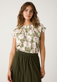 Floral blouse in green with pink and beige patterns; short sleeves; pleated olive skirt with a wide waistband. Lightweight fabric, relaxed fit.