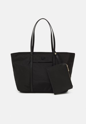 Sac cabas noir avec longues poignées et pochette zippée attachée, avec un logo discret à l'avant, présenté sur fond blanc.