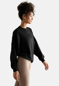 Sweatshirt noir surdimensionné avec un col rond et des manches longues. Texture de tissu douce avec un léger branding sur la poitrine.