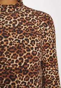 Dlouhý rukáv top z elastického materiálu s hnědým a béžovým leopardím vzorem a vysokým výstřihem. Viditelné texturované detaily.