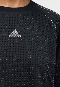 Camiseta deportiva negra de Adidas con pequeñas tachuelas reflectantes que cubren la tela y el logo de Adidas en el pecho.