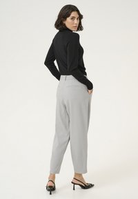 Haut col roulé noir ajusté, pantalon tailored gris clair avec des poches détaillées, et mules à talons noires. Textures lisses et design moderne.