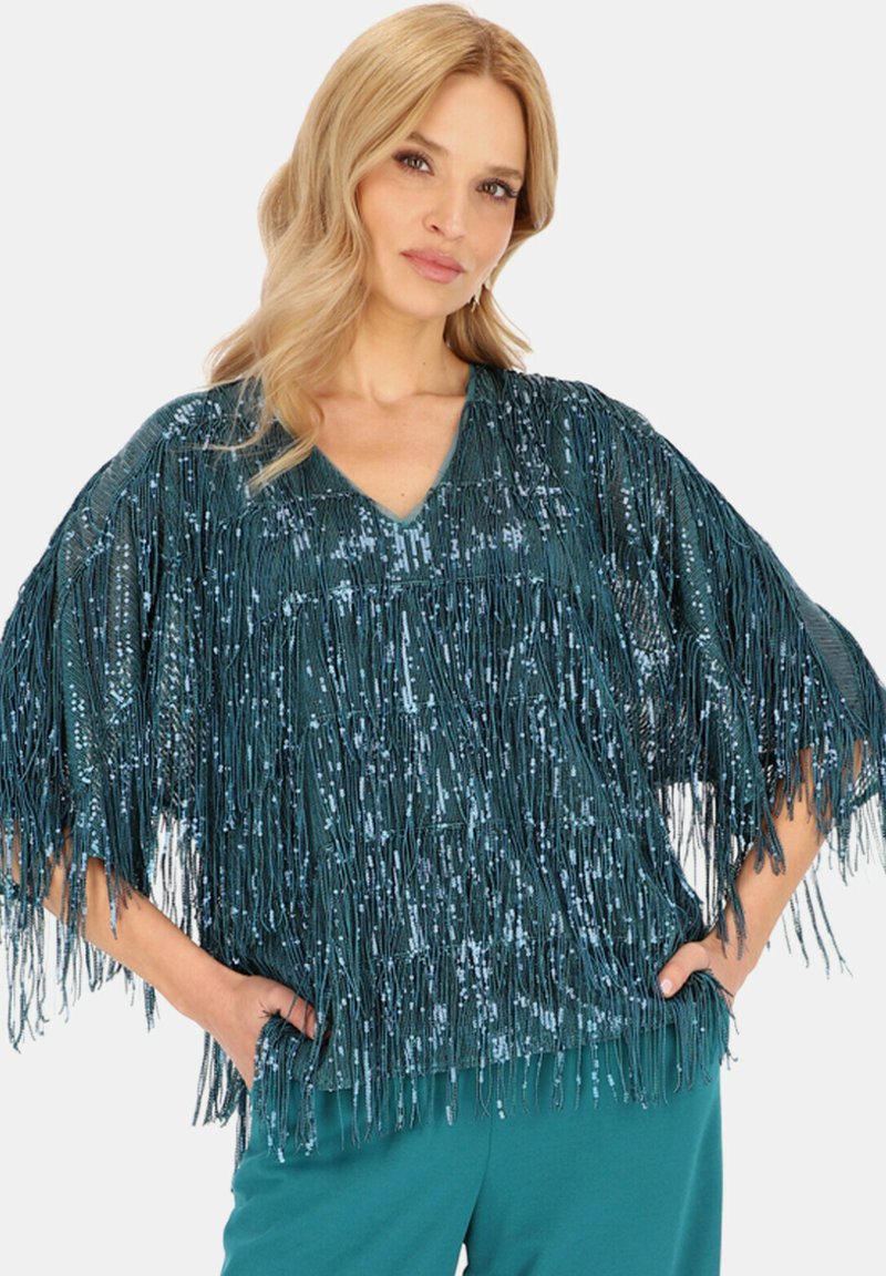 Turkusowa bluzka z frędzlami i dekoltem w kształcie litery V, zdobiona cekinami dla uzyskania tekstury oraz luźnym krojem. Widoczne kieszenie boczne w pobliżu dołu.