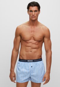 Shorts de boxeur à carreaux bleu et blanc avec une taille marine arborant le logo "BOSS". Matière en coton, coupe décontractée et taille élastique.