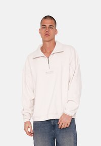Lyserød fleece pullover med kvart lynlås, der har høj krave, afslappet pasform og subtilt logo på brystet.