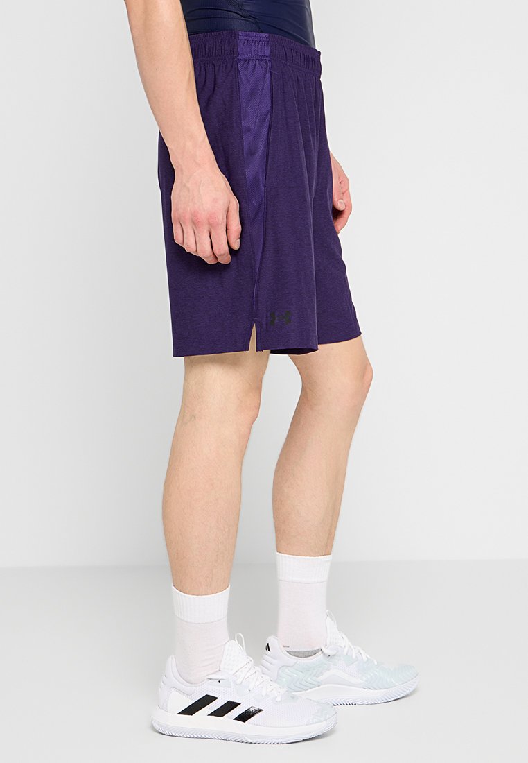 Pantaloni sportivi viola con design a rete, vita elasticizzata, spacco laterale e logo nero sulla parte anteriore inferiore. Indossati con scarpe da ginnastica bianche.
