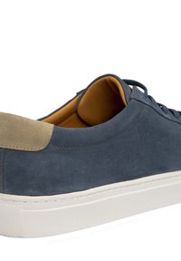 Baskets en suede navy pour homme avec un tablier beige à l'arrière, semelle en caoutchouc blanc et lacets assortis. Doublure intérieure douce de couleur beige.