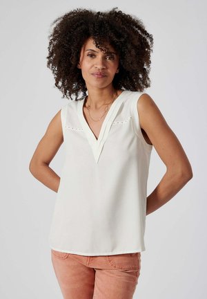 Débardeur blanc sans manches avec un col en V, présentant des découpes subtiles et une texture lisse, associé à un pantalon rose clair.