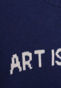 Navyblauer Strickpullover mit dem Text "KUNST IST" in weißen, blockartigen Buchstaben, aus strukturiertem Stoff und mit einem gerippten Halsausschnitt.