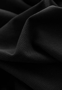 Close-up of soft, black textured fabric with visible knit pattern and gentle folds creating shadows and depth.