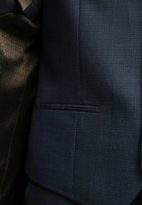 Marineblaues Suit-Jackett aus Stoff mit einem dezenten strukturierten Muster, ausgestattet mit einer Brusttasche und einem kontrastierenden, gemusterten Innenfutter.