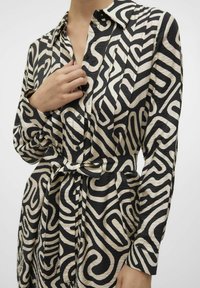 Abito button-up nero e crema con un motivo a spirale geometrica, maniche lunghe, vita con cinturino e tessuto testurizzato.