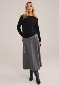 Czarny sweter z długim rękawem zestawiony z szaro-skalowym midi spódnicą z srebrnym łańcuchem na talii. Modelka ma na sobie czarne kozaki do kolan.