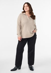 Bež pleteni pulover s ovratnikom, koji ima kabelske uzorke i dugačke rukave, u kombinaciji sa crnim širokim hlačama i crnim čizmama s potpeticom.