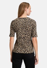 Haut à imprimé léopard avec des manches courtes, présentant une couleur de base beige et des taches noires. Texture lisse avec un col rond.