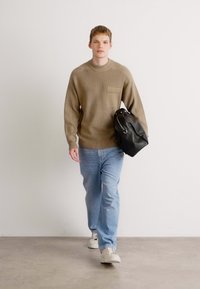 Brown textured sweater with a front pocket, light blue jeans, and gray sneakers; carrying a black leather shoulder bag.