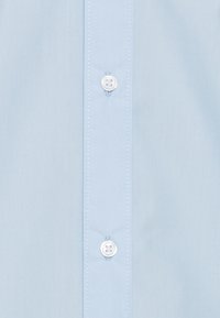 Camicetta azzurra chiara con texture liscia, caratterizzata da bottoni bianchi lungo il davanti e dettagli di cucitura delicati.