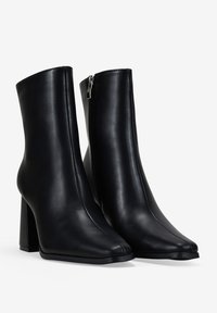 Botas negras de tobillo hechas de cuero suave, con punta afilada, cierre de cremallera en el lateral y un tacón alto y robusto.