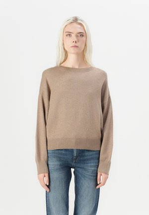 Bruine, gebreide trui met een brede halslijn, drop schouders en een geribbelde zoom. Combinatie met blauwe, rechte jeans.