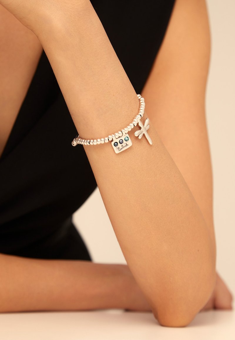 Pulsera de cuentas plateadas con un colgante rectangular que presenta tres piedras azules y grabado, además de un adorno de libélula plateada.