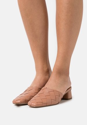 Mules tejidos en cuero color marrón claro con punta afilada y tacón bajo tipo bloque. La superficie texturizada añade interés visual y dimensión.