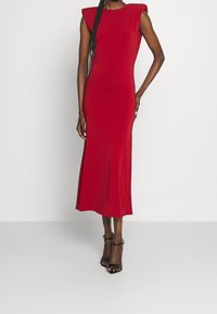 Robe midi rouge avec épaulettes structurées, texture douce et silhouette cintrée. Présente un col rond et descend jusqu'au mi-mollet.