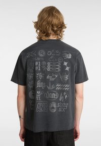 Grå t-shirt med korta ärmar som har olika tryckta logotyper och grafik i ljusare grå toner på baksidan.