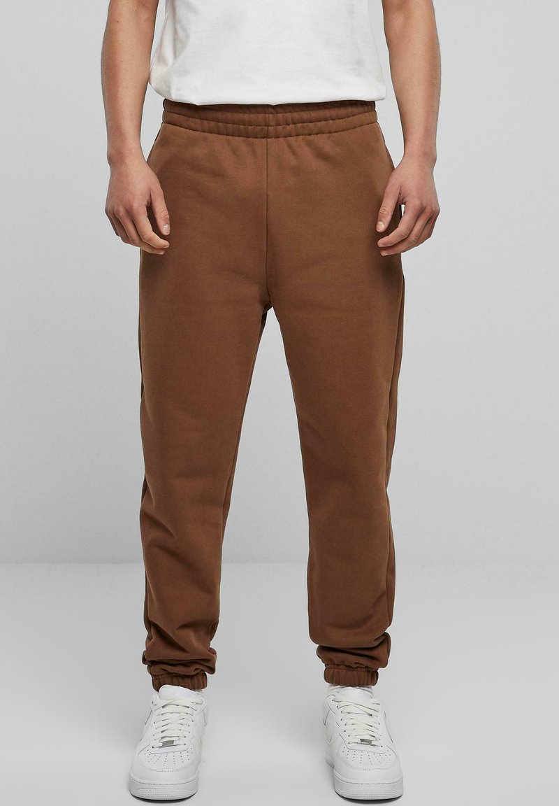 Bruine katoenen joggingbroek met een taps toelopend ontwerp, elastische tailleband en cuffs, gecombineerd met witte sneakers.
