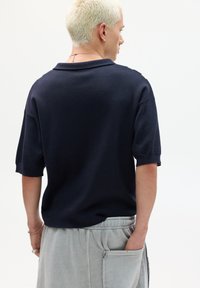 Marineblaues Kurzarm-Polohemd aus Strick mit lockerer Passform, klassischen Kragen und subtiler gerippter Textur an den Ärmeln.