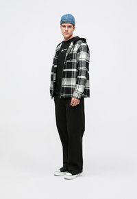 Jachetă din flanel în carouri alb-negru peste un hanorac negru, pantaloni negri și adidași negri cu talpă albă; șapcă din denim.