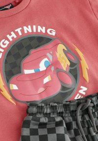 Sweatshirt rouge avec motif de la voiture Lightning McQueen et pantalon à taille élastique noir-gris à carreaux avec cordon de serrage.
