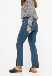 Jeans de mezclilla azul de cintura alta con corte recto, que cuentan con una abertura en el lateral del dobladillo, combinados con una blusa de manga larga a rayas en blanco y negro.