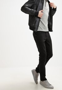 Černá kožená bomber bunda přes šedé tričko, spárovaná s černými slim-fit kalhotami a šedými teniskami. Hladké materiály a elegantní design.