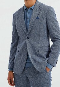 Blå blaser med fiskbensmönster, parat med en ljusblå polo och matchande texturerade byxor. Har slagna lapeller och två knappar.