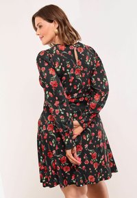 Juoda gėlėta suknelė, pagaminta iš minkštos medžiagos, turinti ilgas rankoves, raktinės skylutės nugarą ir raudonas gėles su žaliomis lapėmis.