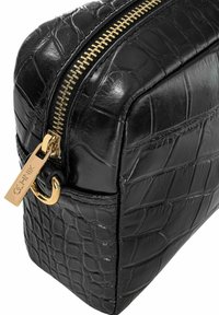Czarna torba ze skóry wytłaczanej w węża z złotym zamkiem błyskawicznym, prostokątny kształt i złota metka. Gładka tekstura z wyraźnym wzorem.