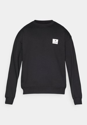 Sweatshirt noir avec un col ras du cou, des poignets et un ourlet côtelés. Présente une patch carrée blanche avec le texte "snow peak" en haut à gauche.