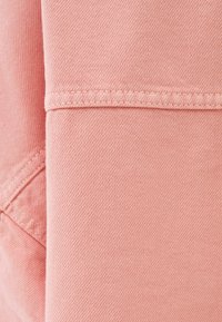 Ljust rosa denimtyg med en mjuk textur, med ett diagonalt vävmönster och prydliga sömmar längs kanterna.