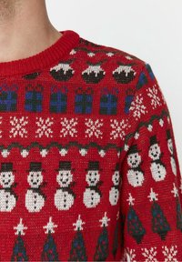 Red knitted sweater featuring snowmen, Christmas trees, and gift patterns in white, green, and blue. Ribbed crew neckline. Medium texture.