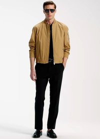 Beež bomberjakk soonikkoes varrukate ja alaäärega, mida kantakse musta särgi ja pükstega. Mustad kingad ja päikeseprillid lõpetavad komplekti.