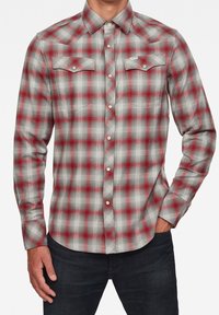 Camisa de cuadros roja y gris, abotonada, con mangas largas, dos bolsillos en el pecho y cuello puntiagudo, fabricada con tejido ligero.