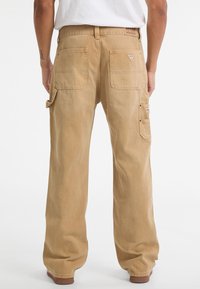 Khaki Baumwoll-Cargohosen mit geradem Bein. Verfügt über mehrere Taschen, ein Logo-Patch auf der Rückseite und eine lockere Passform.