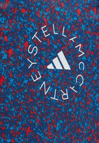 Tela de patrón azul y rojo con un logo circular blanco central que presenta texto estilizado y un emblema de tres franjas. Textura suave.
