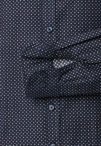 Navy button-up shirt featuring a small geometric pattern in white and blue, with a textured fabric, two-button cuffs, and a classic collar.