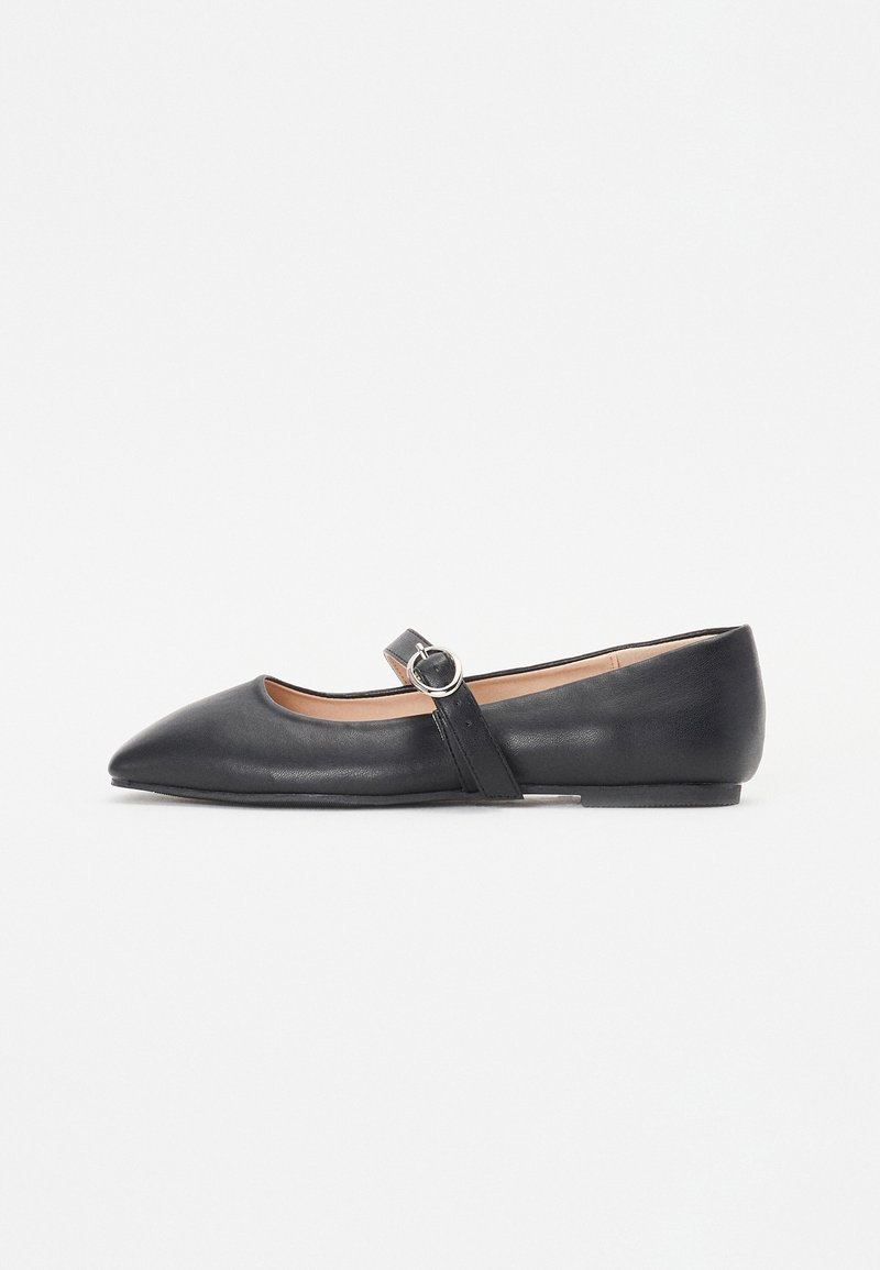 Chaussure plate Mary Jane en cuir noir avec bout pointu et bride à boucle argentée sur fond blanc uni.