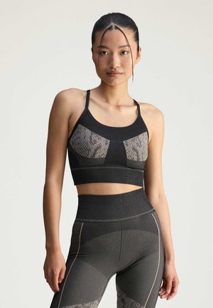 Black sports bra with fitted design, featuring snake print front panel and adjustable straps. Paired with high-waisted black leggings with accents.