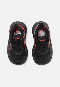 Zapatos deportivos negros con detalles rojos, parte superior de malla, diseño texturizado, punta redonda y cierre con cordones. Logo visible en la lengüeta.